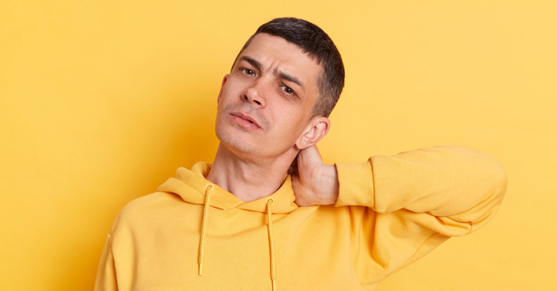 Worried anxious man wearing casual style hoodie, posing isolated over yellow background, touching neck, feeling acute pain moving and turning head