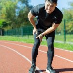 Asian man bending down while holding leg because of knee pain