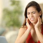 Young woman sitting at desk holding jaw because of pain