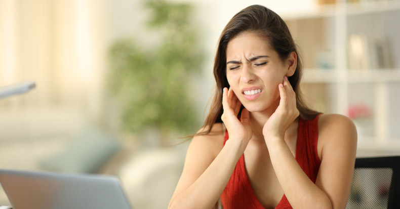 Young woman sitting at desk holding jaw because of pain